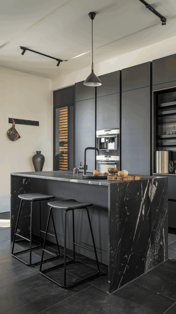 Modern kitchen with dark cabinetry and an island featuring a black marble countertop, equipped with two black stools, built-in oven, and a pendant light above.